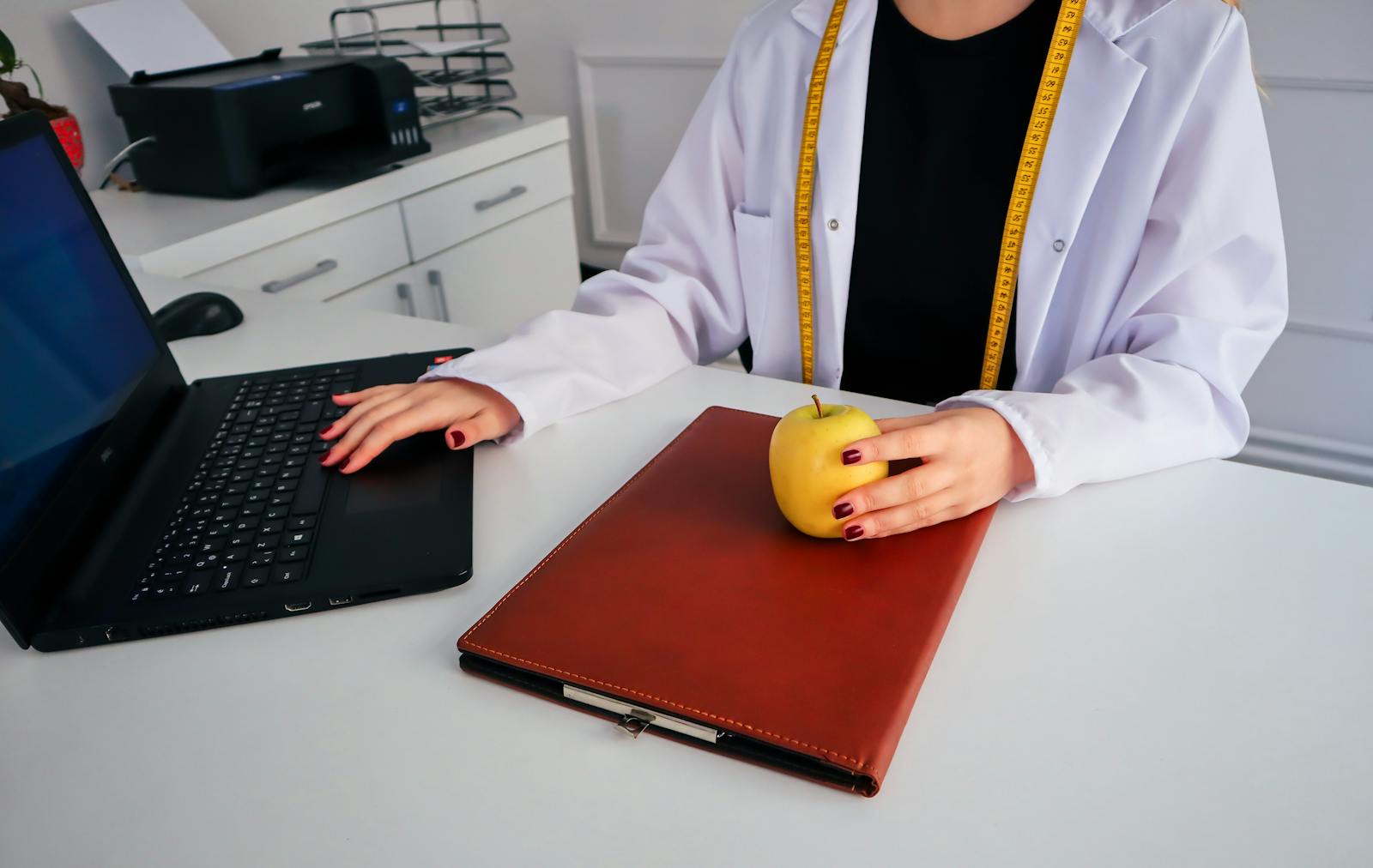 A dietician sitting at a desk with a laptop and apple, symbolizing healthy working lifestyle.